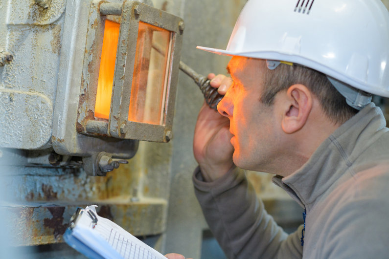 Man looking through inspection glass of industrial incinerator