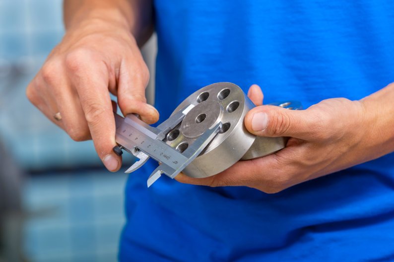 Using calipers to measure dimensions of metal part